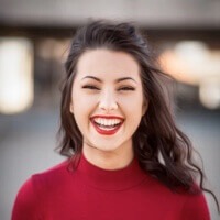 Woman with dark hair wearing a red sweater, smiling at the camera.